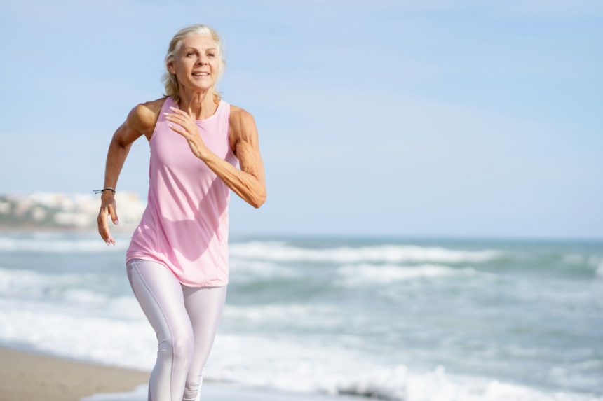 Mature woman running along the shore of the beach. Older female doing sport to keep fit