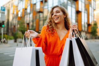 Stylish young woman with shopping bags walking down sunny street in bright dress. Concept of sales.